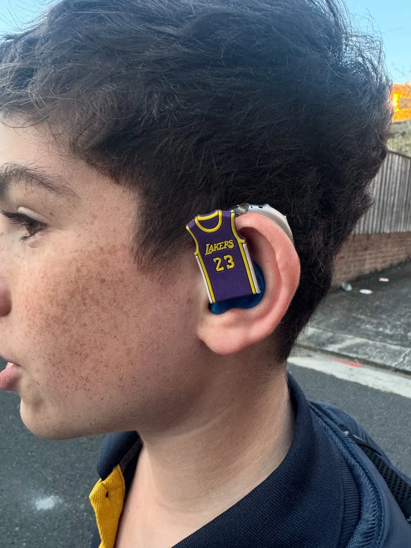 A basketball jersey charm clipped onto a hearing aid, seen close up from the side