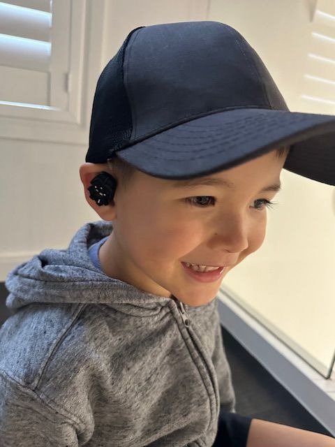 A boy in a cap wearing a hearing aid with a black charm