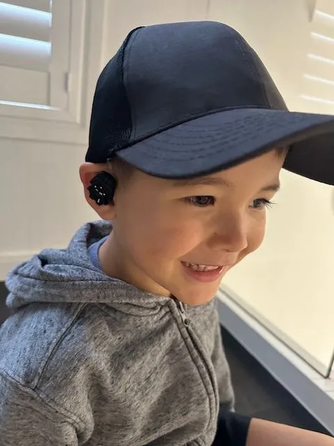 A boy in a cap wearing a hearing aid with a black charm